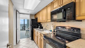 A kitchen with wooden cabinets, a black microwave, a stove, and a refrigerator. - Caribbean Resort Unit 732 (Myrtle Beach)