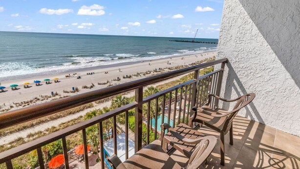 A balcony with a view of the beach and ocean, outdoor furniture, and umbrellas. - Caribbean Resort Unit 732 (Myrtle Beach)