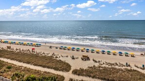 A beach with rows of colorful umbrellas and beach chairs, a sandy path, and a clear view of the ocean. - Caribbean Resort Unit 732 (Myrtle Beach)