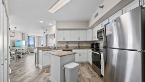 A modern kitchen with white cabinets, a stainless steel refrigerator, and a wooden island with stools. - Bluewater 601 with Balcony (Orange Beach)