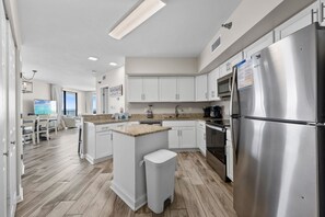 A modern kitchen with white cabinets, a stainless steel refrigerator, and a wooden island with stools. - Bluewater 601 with Balcony (Orange Beach)