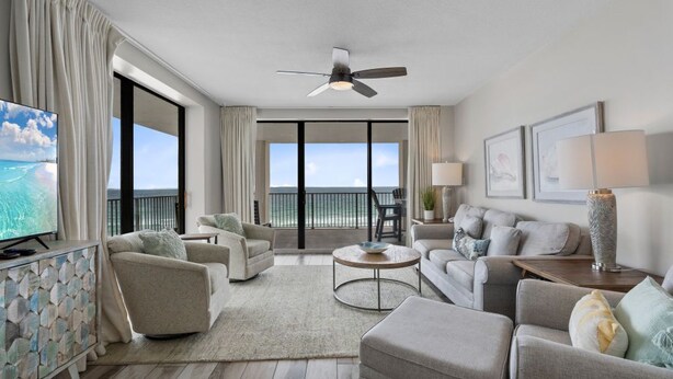 A modern living room with a balcony, a ceiling fan, and a television. - Bluewater 601 with Balcony (Orange Beach)