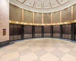A spacious lobby with a checkered floor, a central column, and a ceiling with a geometric pattern.