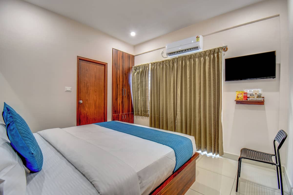 Une chambre à coucher comprenant un lit, un téléviseur fixé au mur, un climatiseur, une porte en bois et une chaise.