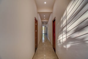 A hallway with a tiled floor, wooden doors, and a wall with a patterned design. - AVN Comforts Mysore (Mysore)