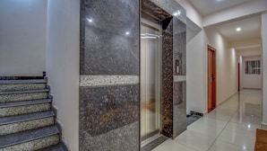 A modern interior with a marble staircase, a glass elevator, and a hallway leading to a door. - AVN Comforts Mysore (Mysore)