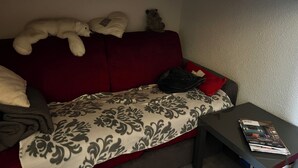 A red sofa with a patterned throw, a small table with a magazine, and a teddy bear on the sofa. - Studio les arcs ski pied immeuble (Bourg-Saint-Maurice)