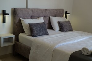 A neatly made bed with white and gray bedding, a headboard, and two bedside tables with wall-mounted lamps. - Hotel Abedini (Sarandë)