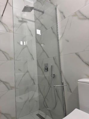 En moderne brusekabine med glasvægge, håndbruser og et kontrolpanel på væggen.