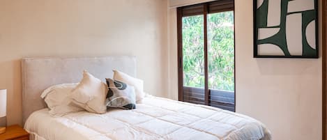 A bedroom with a bed, pillows, a nightstand, a window with blinds, and a wall art piece.