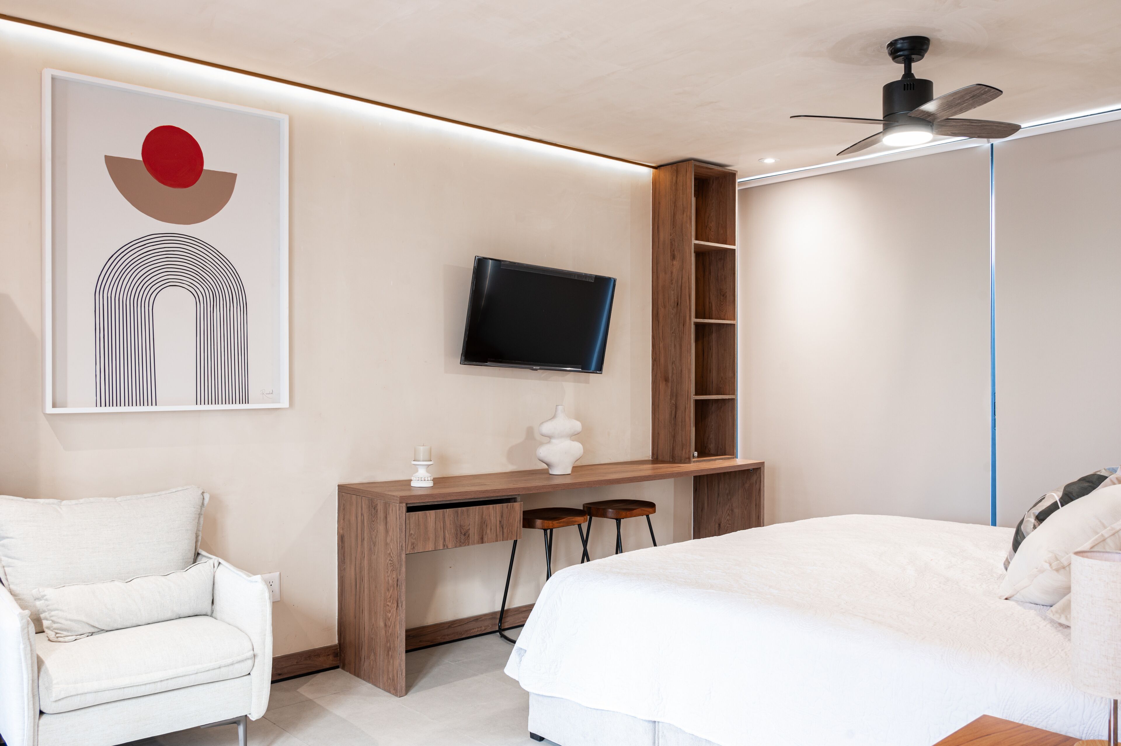 A bedroom with a bed, a desk with a TV, a chair, and a wall art piece.