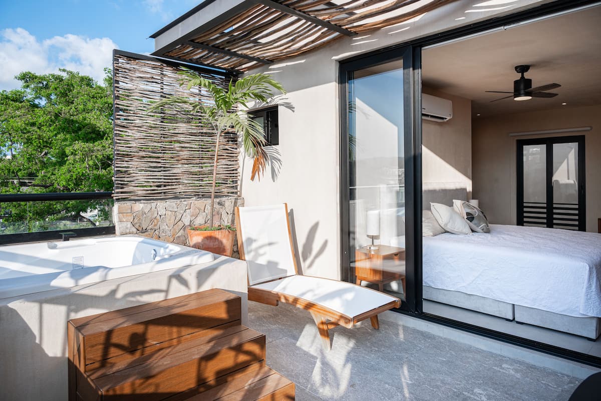 Un dormitorio moderno con una cama grande, un vidrio corredizo que da a un balcón y un jacuzzi.
