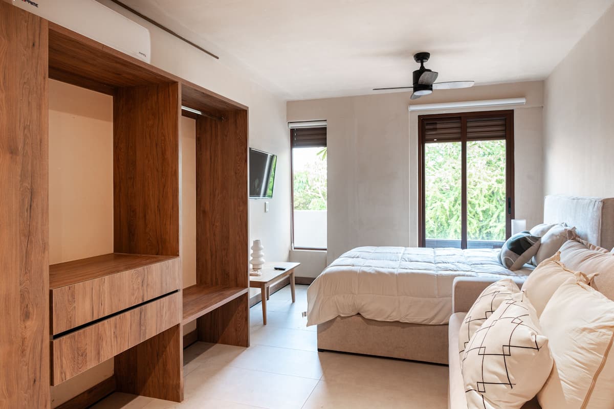 Un dormitorio con cama, armario de madera, televisor y ventana con vista a la vegetación.