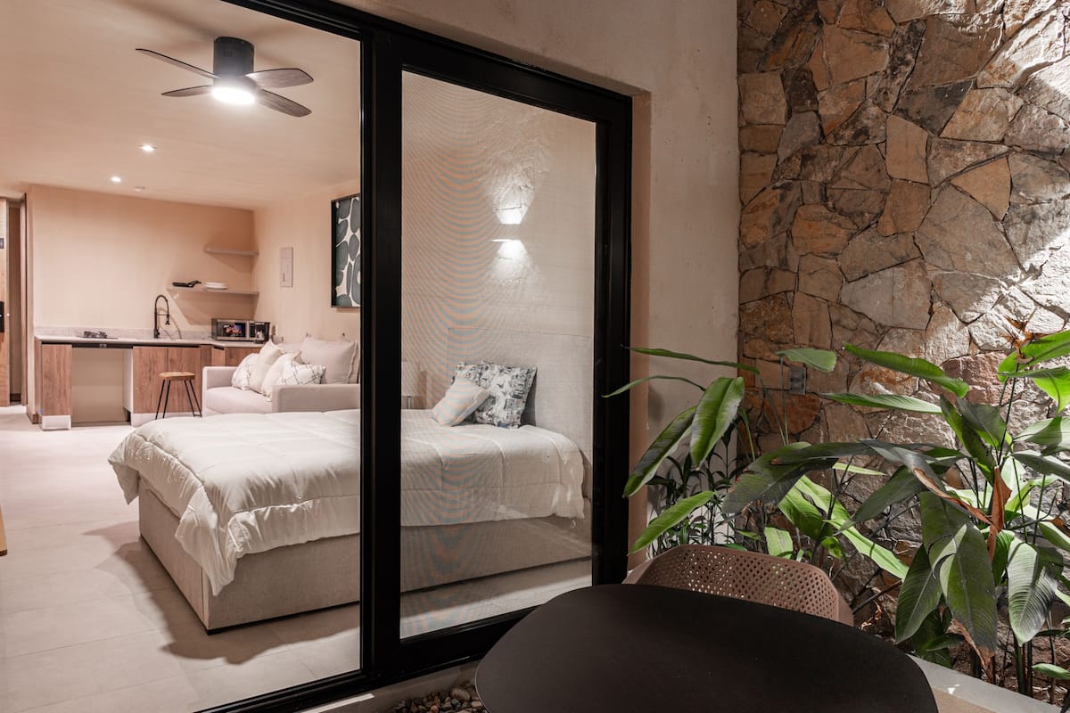 Un dormitorio moderno con una cama grande, un escritorio y vistas a una sala de estar a través de un ventanal.