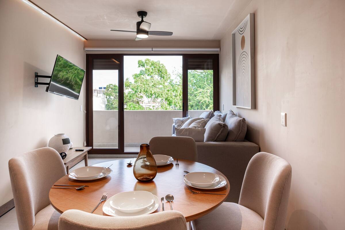 Un comedor con una mesa dispuesta para cuatro personas, un ventilador de techo y un televisor montado en la pared.