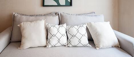 A sofa with four pillows, a framed abstract artwork, and a plain wall.