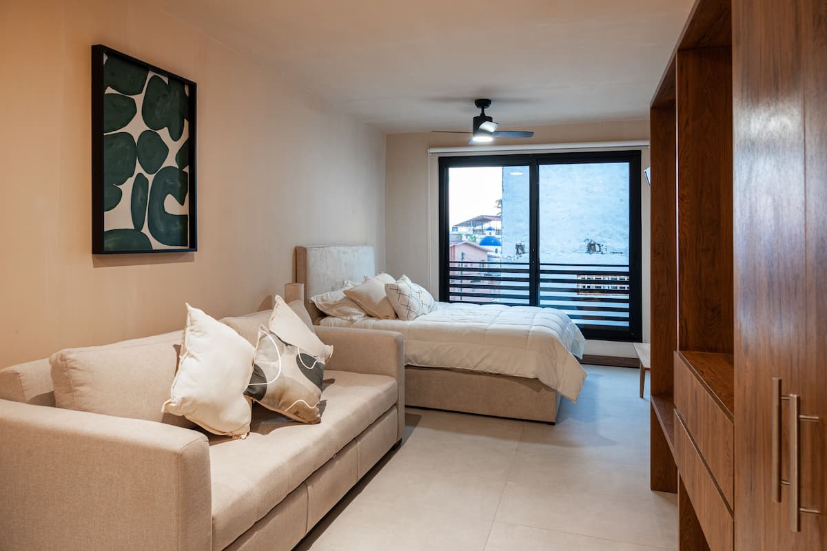 Habitación de hotel con sofá, cama, ventilador de techo y una ventana grande con vistas.