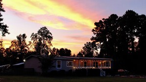 A house with a porch, surrounded by trees, during sunset. - !!POOL!! PEACEFUL FARMHOUSE IN SHALLOTTE! 
5 MINS TO BEACHES AND OUR SWEET TOWN! (Shallotte)