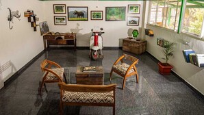 A room with a desk, two chairs, a scooter, and a potted plant. - Vanah Stays (Heggadadevankote)