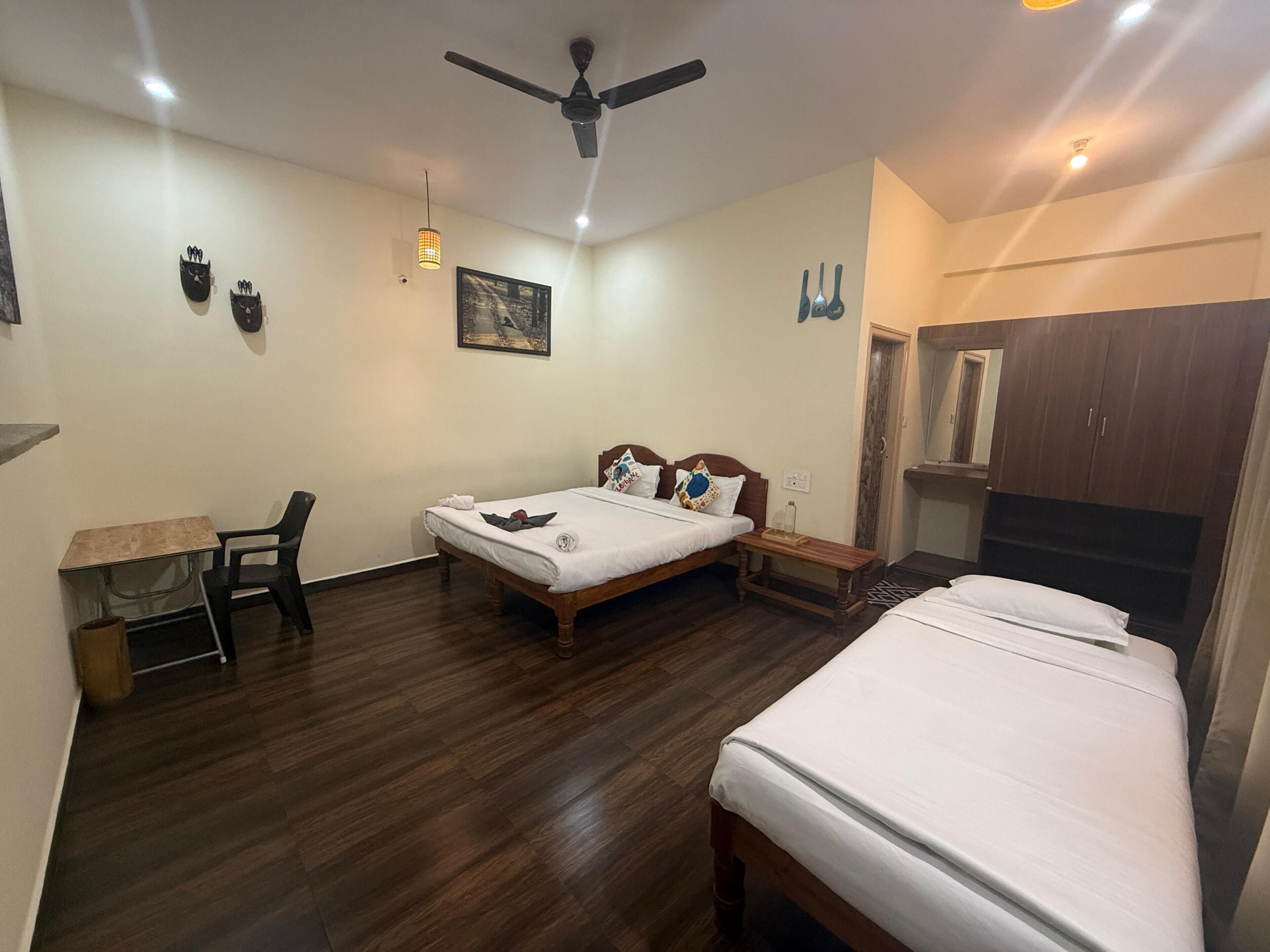 Une chambre d’hôtel avec deux lits, un bureau, une chaise, un ventilateur de plafond et une armoire.