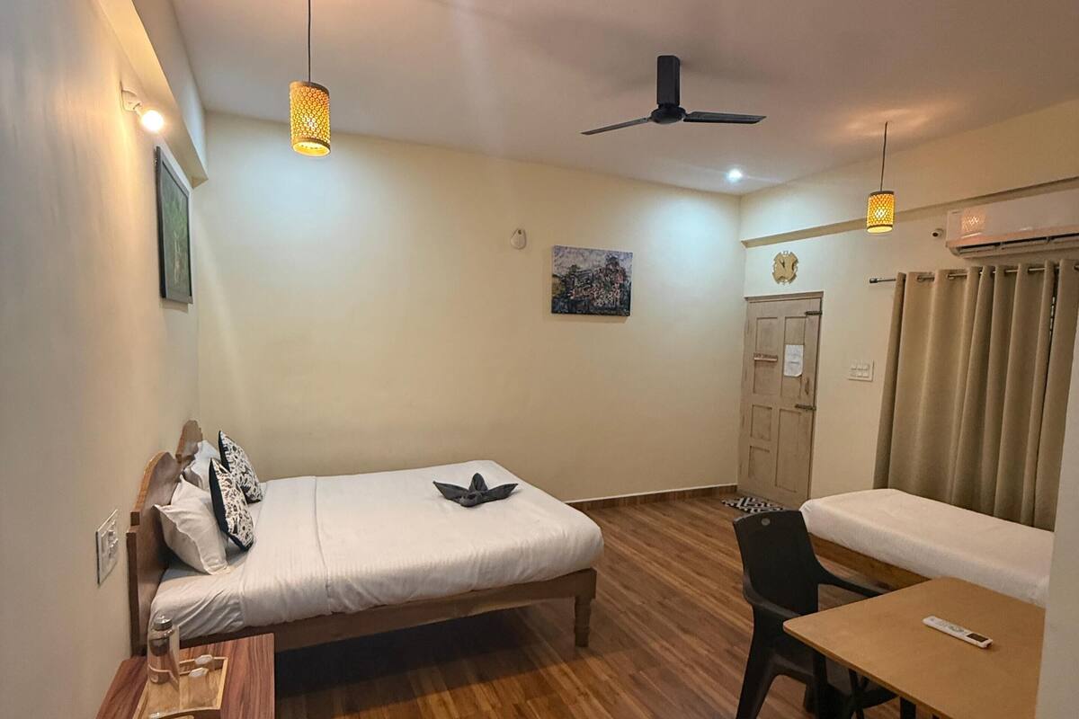 A room with a bed, a desk, a chair, a table, a ceiling fan, and a wall-mounted air conditioner.