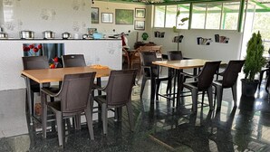 A modern dining area with a counter, chairs, and a view of greenery outside. - Vanah Stays (Heggadadevankote)