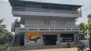 A two-story building with a sign for a camera rental service and wildlife gift store. - Vanah Stays (Heggadadevankote)