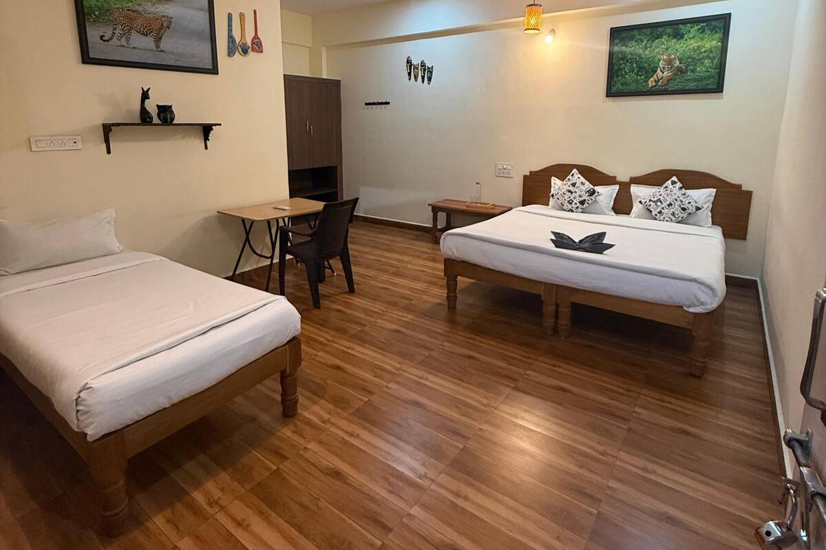 A room with two beds, a ceiling fan, wooden flooring, and wall-mounted artwork.