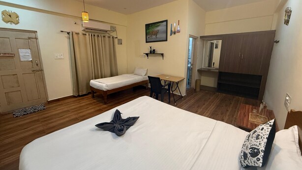 A hotel room with a bed, a desk, a chair, a wardrobe, a ceiling fan, an air conditioning unit, and a painting on the wall. - Vanah Stays (Heggadadevankote)
