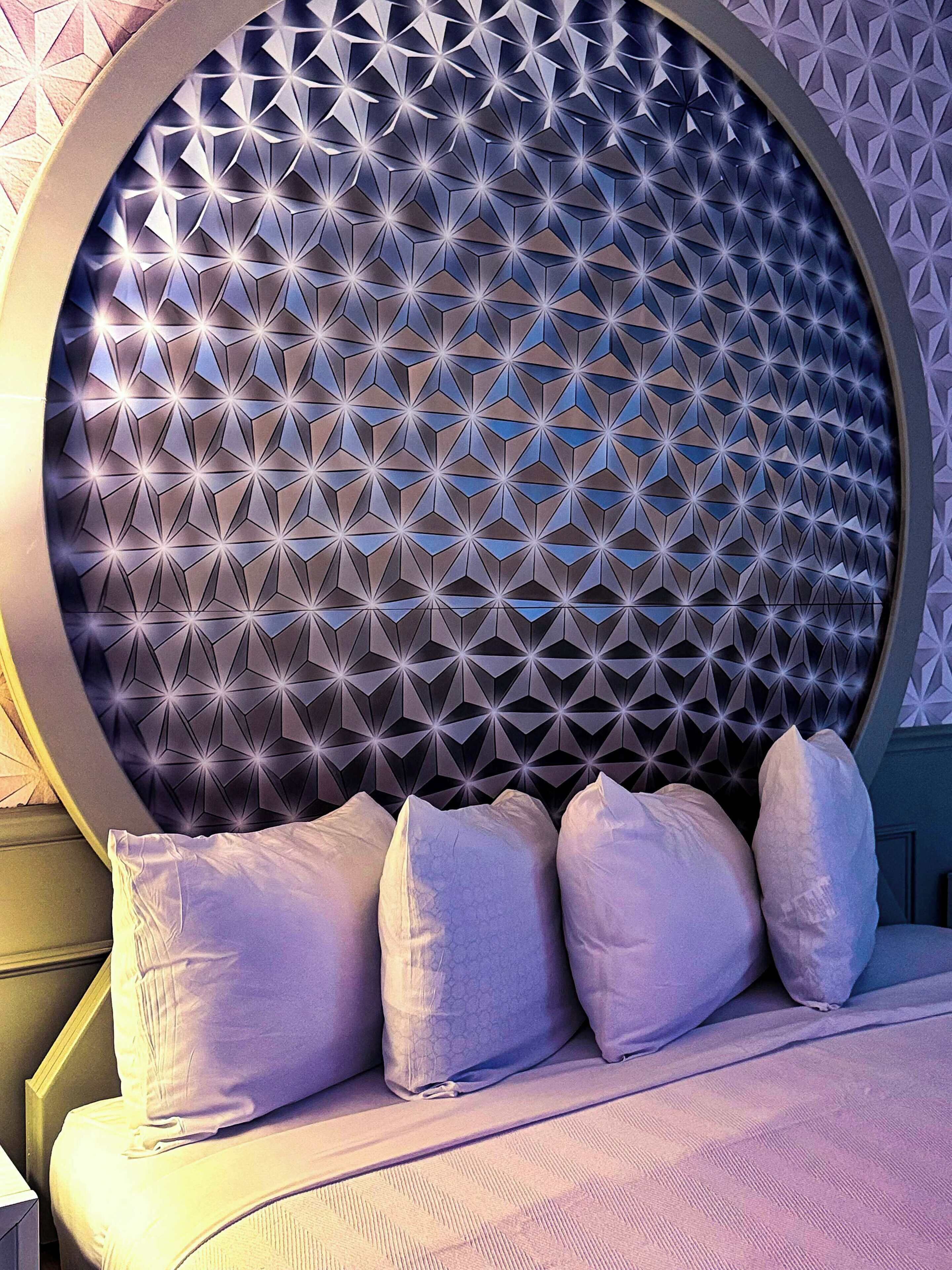 Cabecera circular con un diseño geométrico, una cama con ropa de cama blanca y un arreglo de almohadas.
