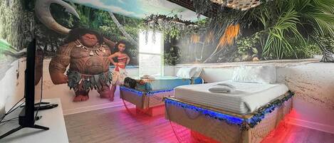 A room with a mural, a bed, a small table, and a TV.