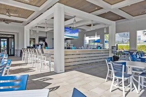 Un espace extérieur aménagé avec des chaises blanches et bleues, un comptoir de bar et un plafond orné de poutres en bois.