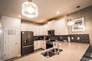 A modern kitchen with white cabinets, stainless steel appliances, a black tiled backsplash, and pendant lighting. - 9BR Fun Villa Sleeps 24 Pool Theater, Themed Near Disney (Four Corners)