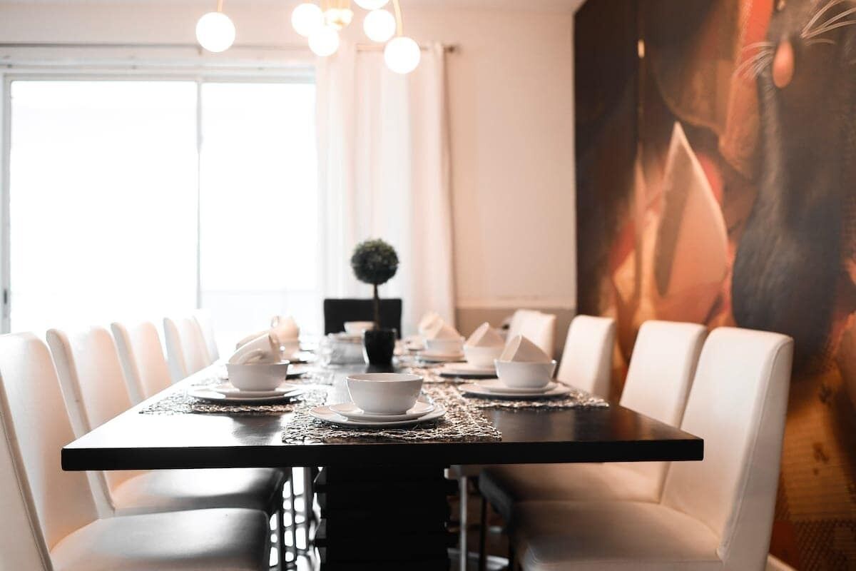 A dining table set with white chairs, a small plant, and a painting on the wall.