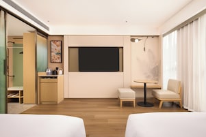 Habitación de hotel con cama, escritorio, silla, televisor y ventana con cortinas.