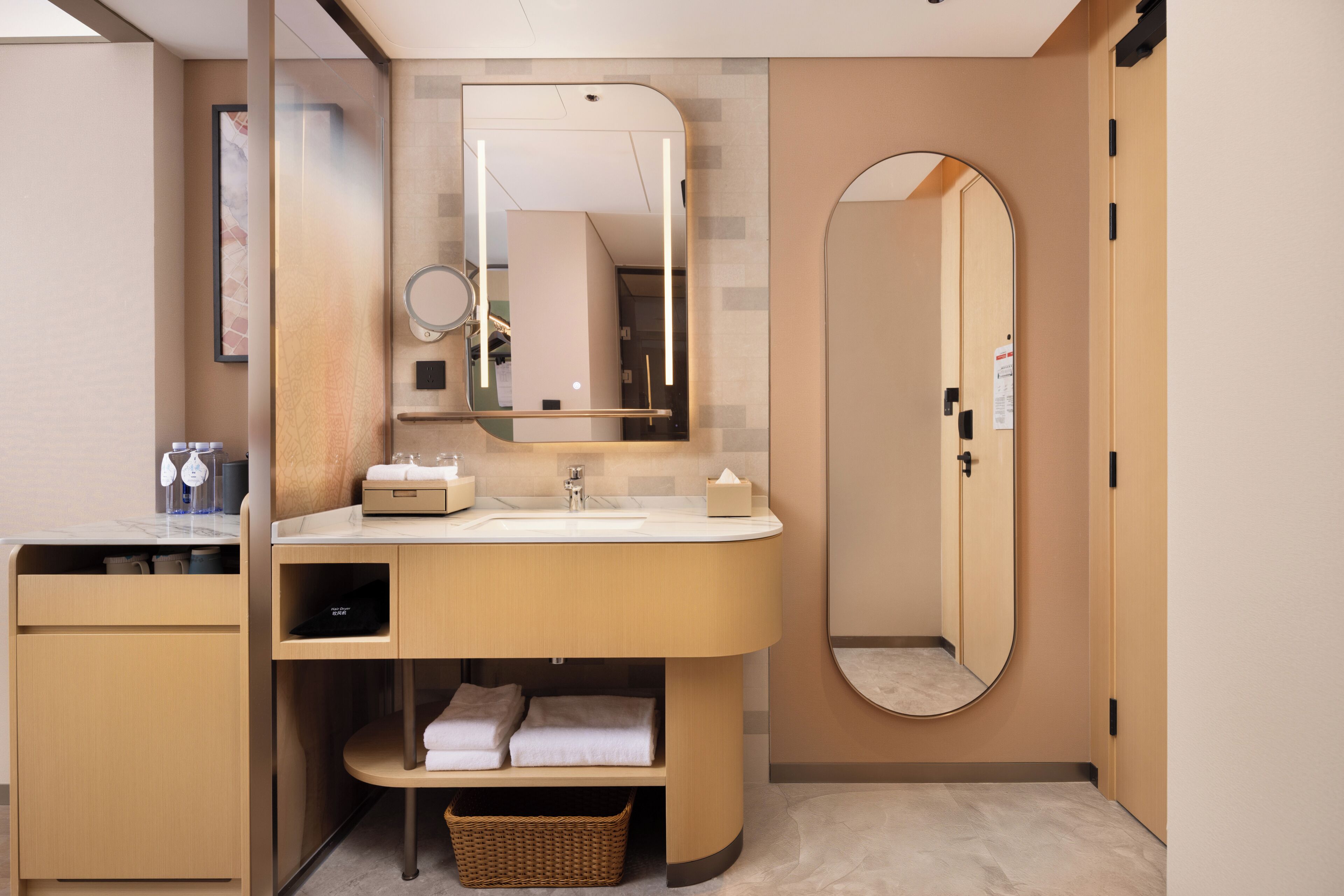 A modern bathroom with a vanity, sink, mirror, and a round mirror above the sink. There is a towel rack and a basket under the vanity.