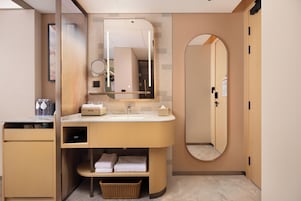 Un baño moderno con tocador, lavabo, espejo y un espejo redondo sobre el lavabo. Hay un perchero y una cesta debajo del tocador.