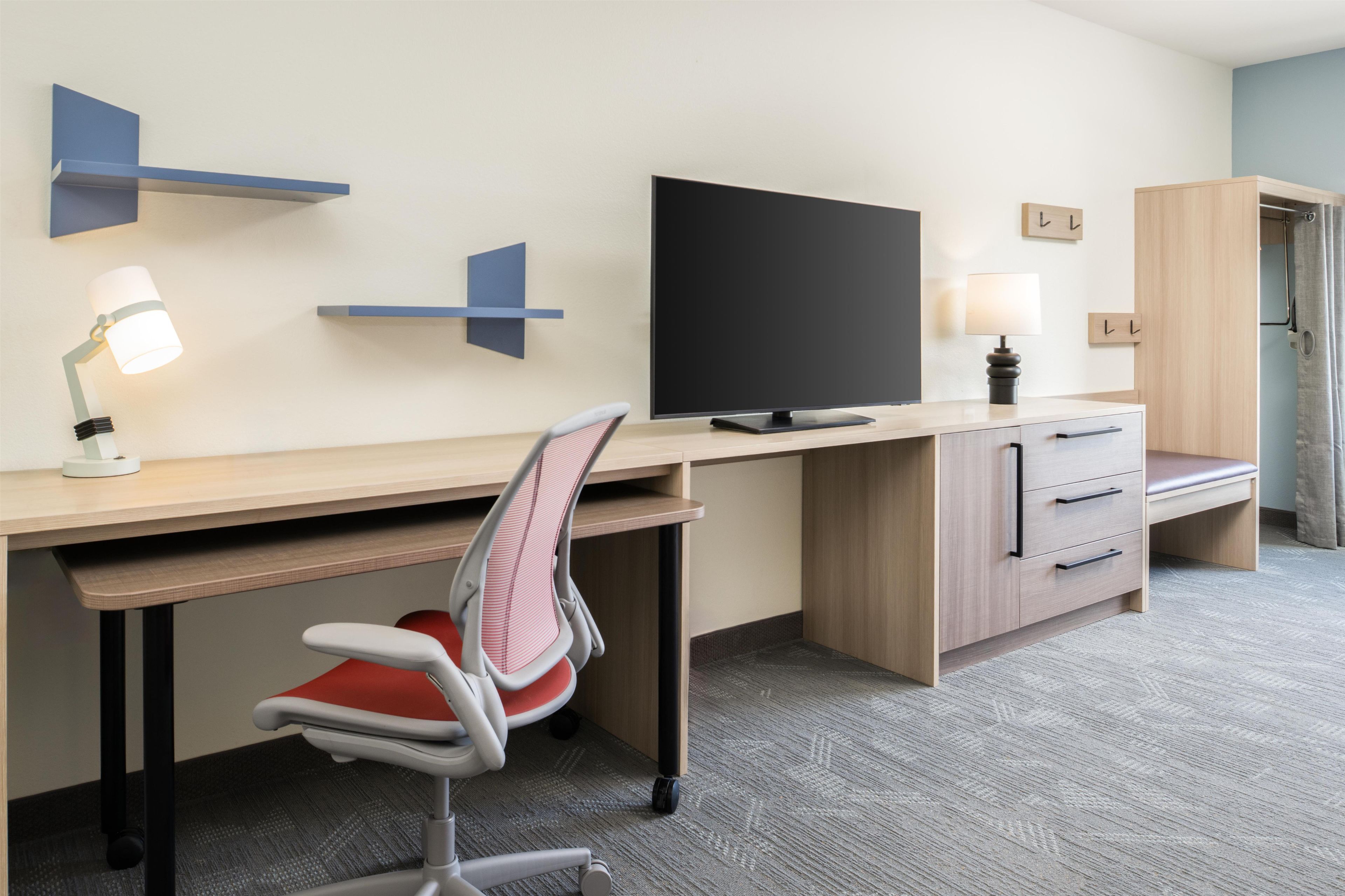 A hotel room with a desk, chair, television, and wardrobe.