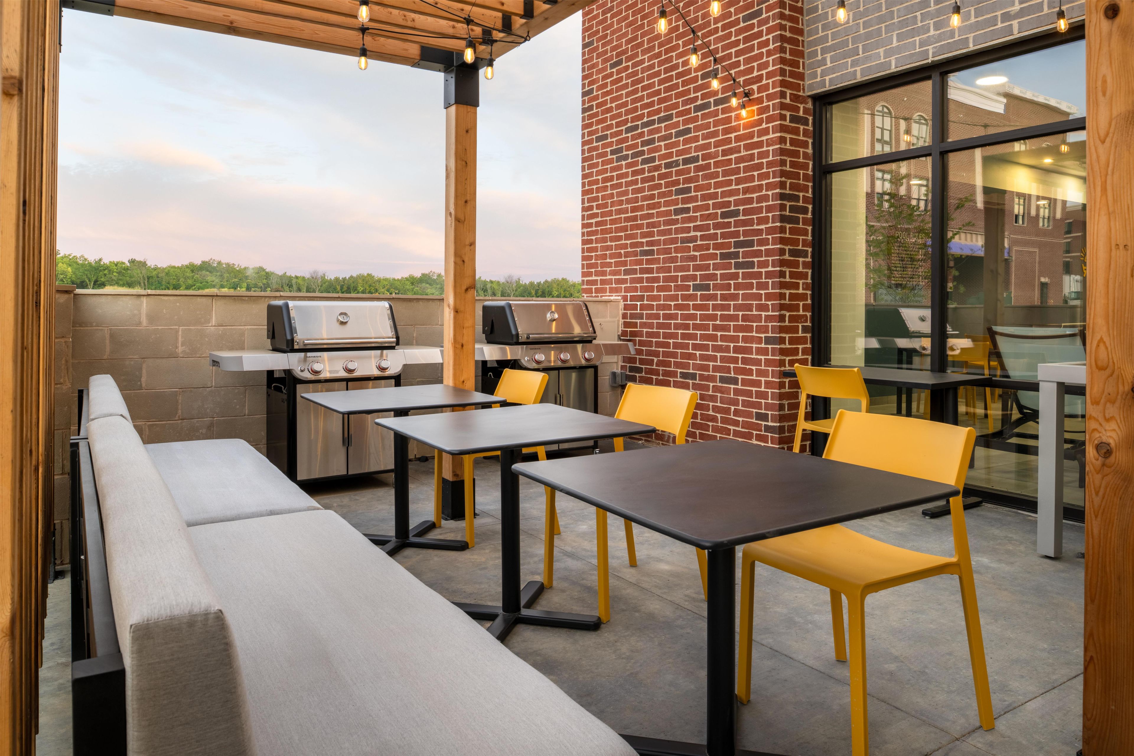 An outdoor patio with a brick wall, two barbecue grills, and seating arrangements.