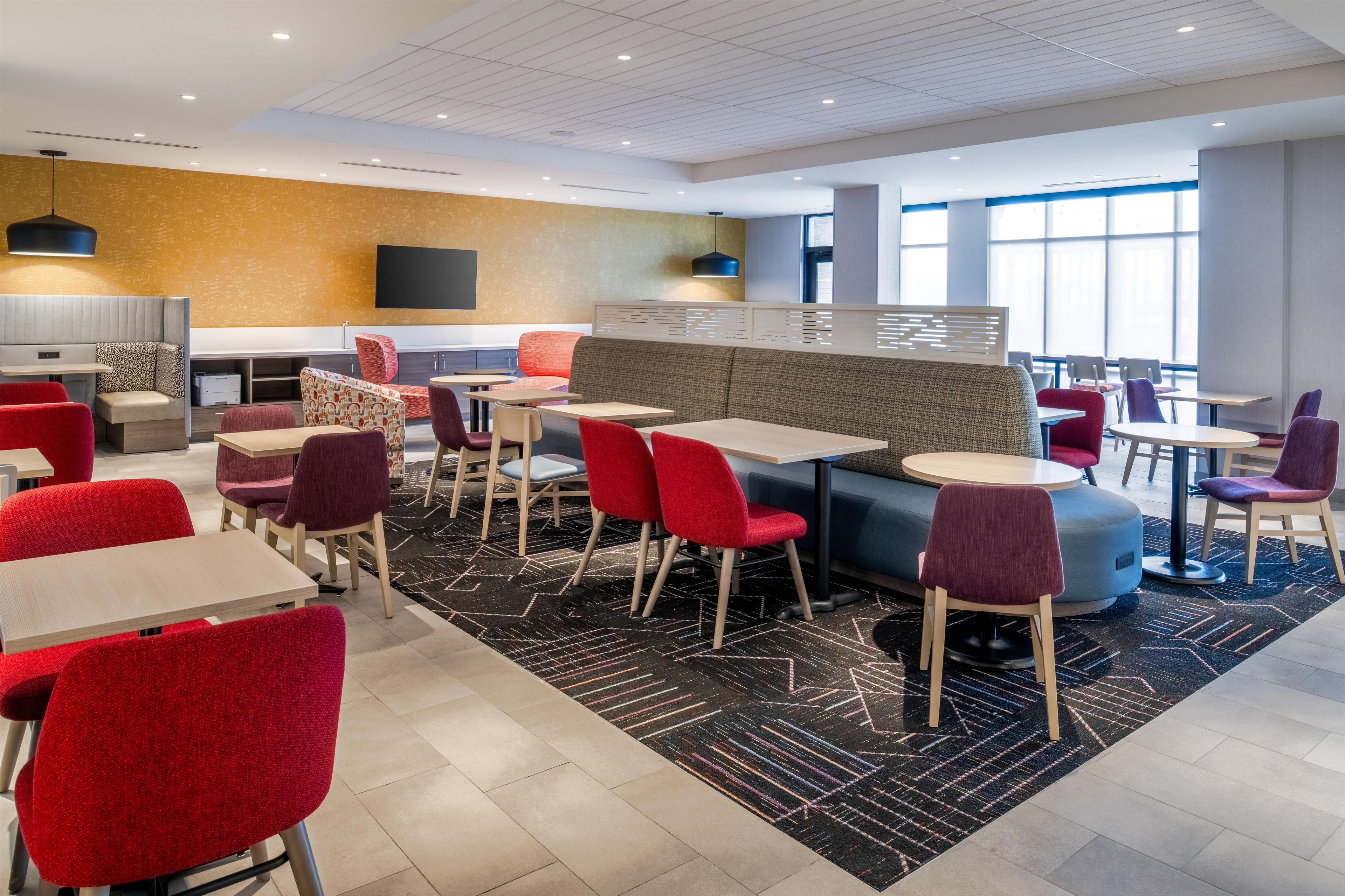 A modern hotel lobby with seating areas, tables, and a large window providing natural light.