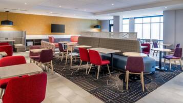 A modern hotel lobby with seating areas, tables, and a large window providing natural light.