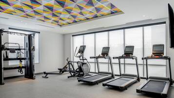 Un gimnasio con cintas de correr, bicicletas estáticas y un techo con un patrón geométrico colorido.