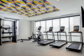 Une salle de sport équipée de tapis de course, de vélos d’exercice et dont le plafond est orné d’un motif géométrique coloré.