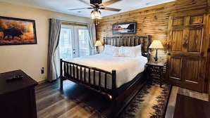 Un dormitorio con cabecera de madera, cama con sábanas blancas, ventilador de techo, un cuadro de un alce y una puerta de madera.