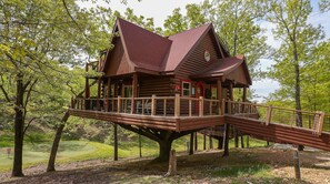 A wooden cabin with a deck, surrounded by trees.