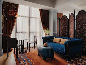 A room with a blue sofa, a wooden chair, a small table with fruit, and a patterned rug. - NoMad Hilton Singapore (Singapore)