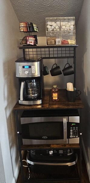 Eine Küche mit Kaffeemaschine, Mikrowelle, hängenden Töpfen und einem Regal mit Büchern und Küchenutensilien.