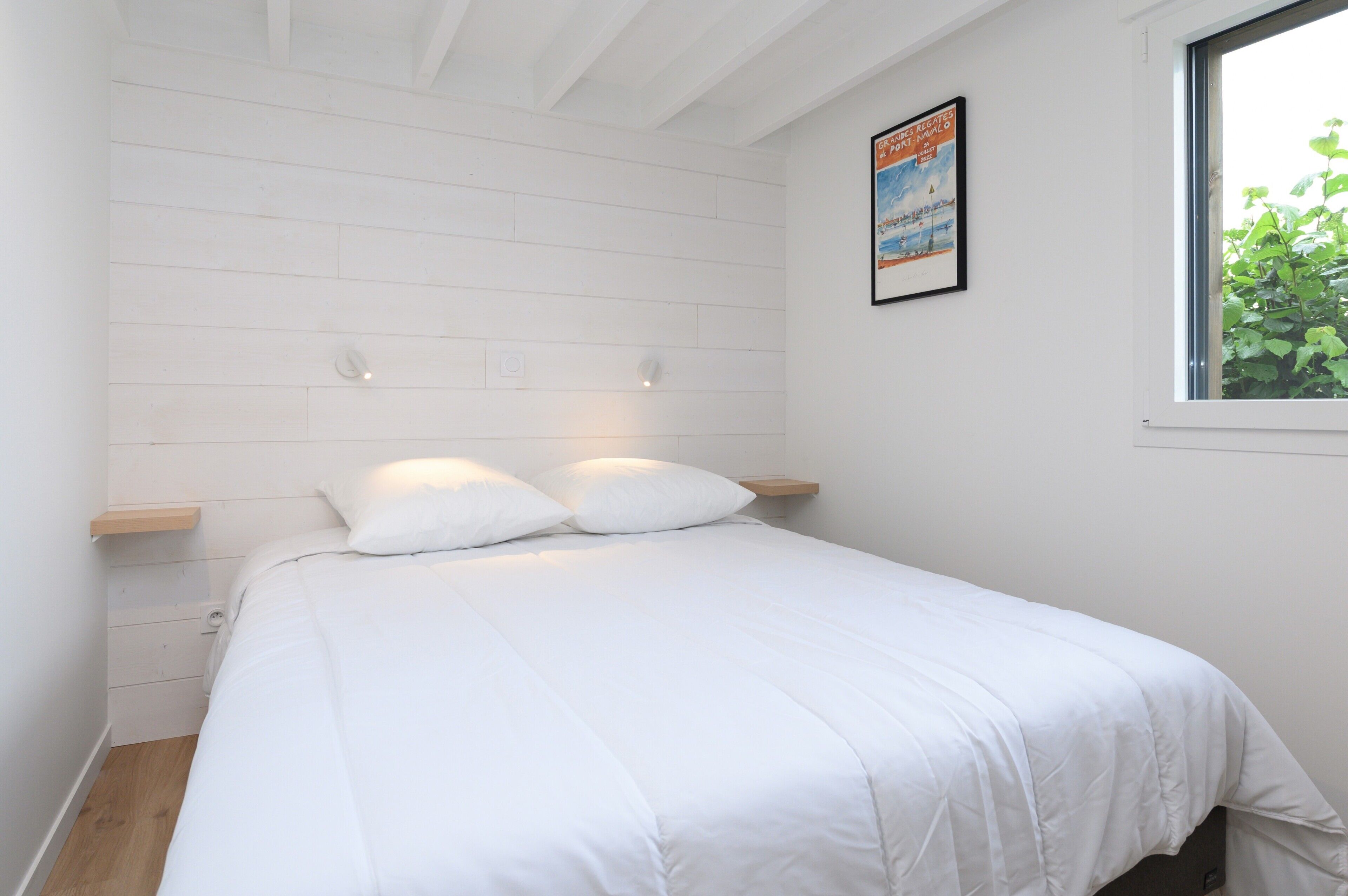 Ein Schlafzimmer mit Bett, weißen Wänden, einem Fenster und einem Bild an der Wand.