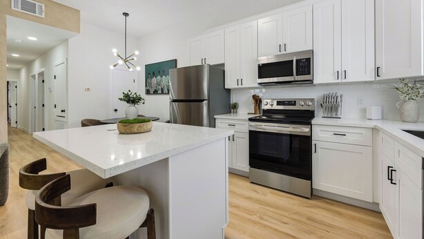 A modern kitchen with white cabinets, stainless steel appliances, a central island with bar stools, and a pendant light. - 3BR Modern Home 15 Min to NRG, Downtown & Hobby (Houston)