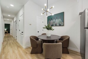 A modern kitchen with a dining area, featuring a round table with chairs, a vase with greenery, and a painting on the wall. - 3BR Modern Home 15 Min to NRG, Downtown & Hobby (Houston)